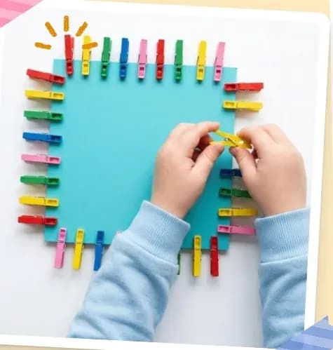 A child's hands pinching coloured pegs onto the edge of a blue card